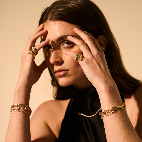 Woman wearing gold jewelry against a beige background