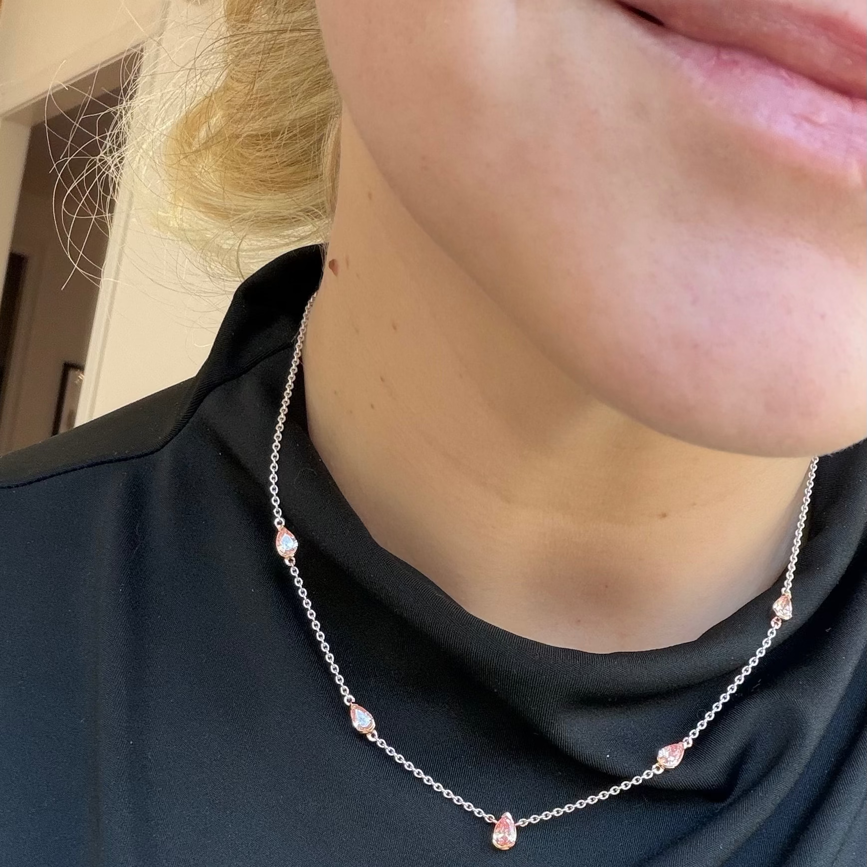 Person wearing a delicate necklace with small pink LAB DIAMONDS against a dark shirt.