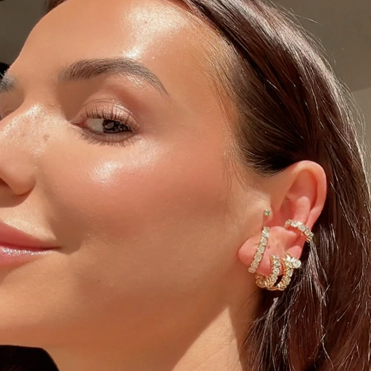 Woman wearing stacked earrings including a lab diamond ear cuff in 14K yellow gold.