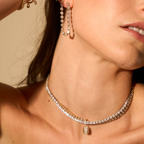 Close-up of a woman wearing a diamond necklace and earrings against a beige background