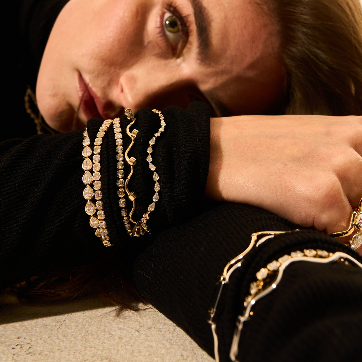 Person wearing gold jewelry including a necklace, bracelet, and ring on a neutral background