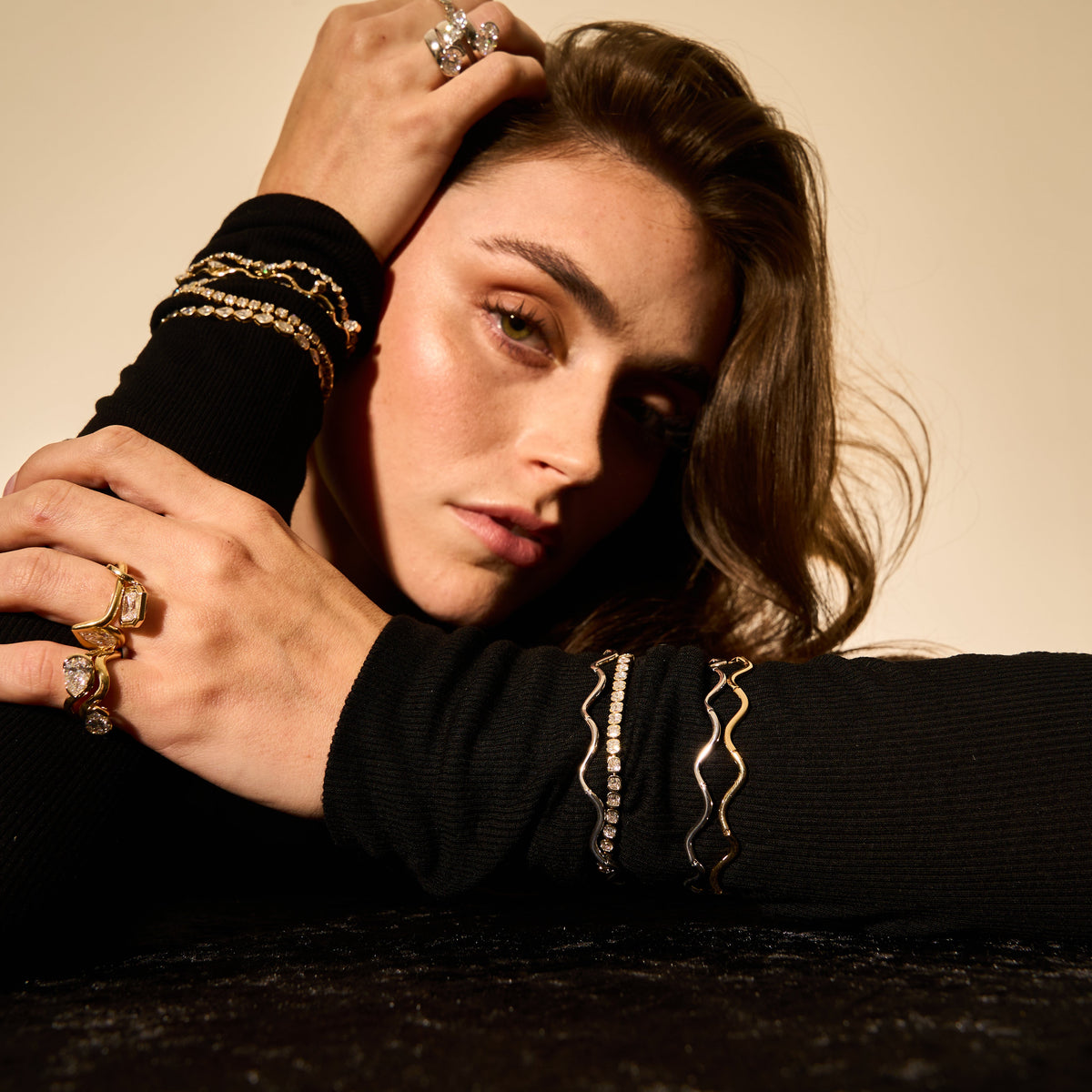 Person wearing multiple rings and bracelets on a neutral background