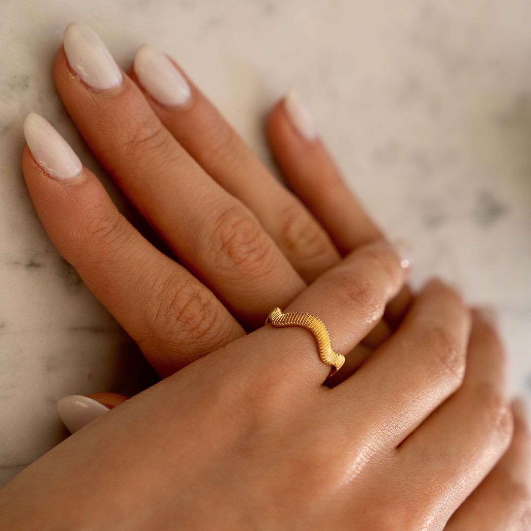 Woman wearing a fluted sculptural ring with ribbed texture while holding a drink.