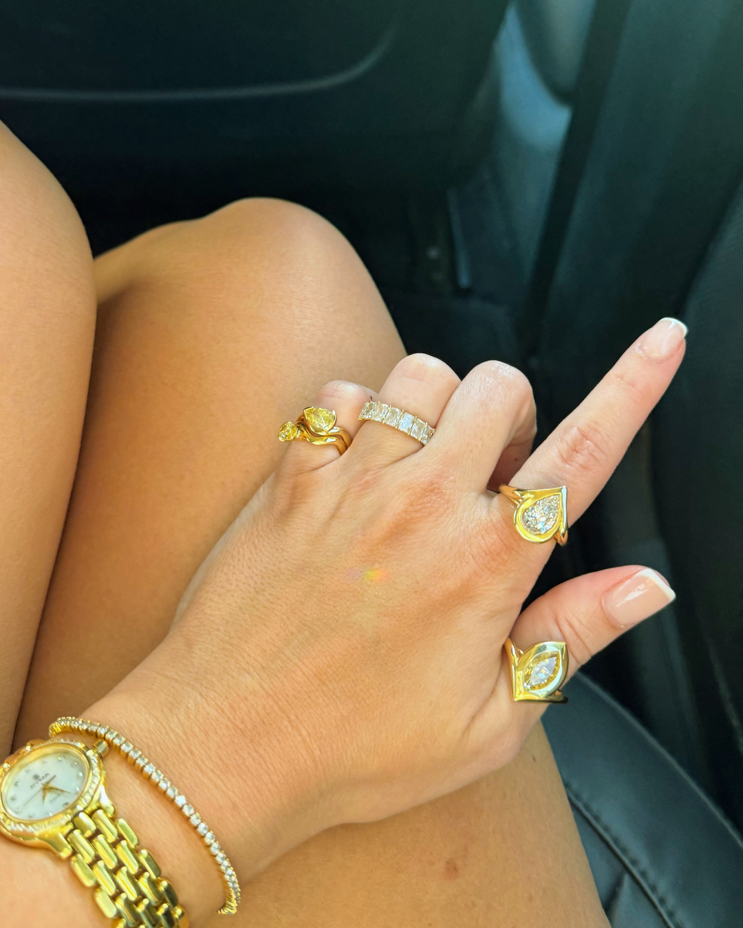 Woman's hand taken in the back of a luxury car showing full ring stack. Every finger is a ring finger.
