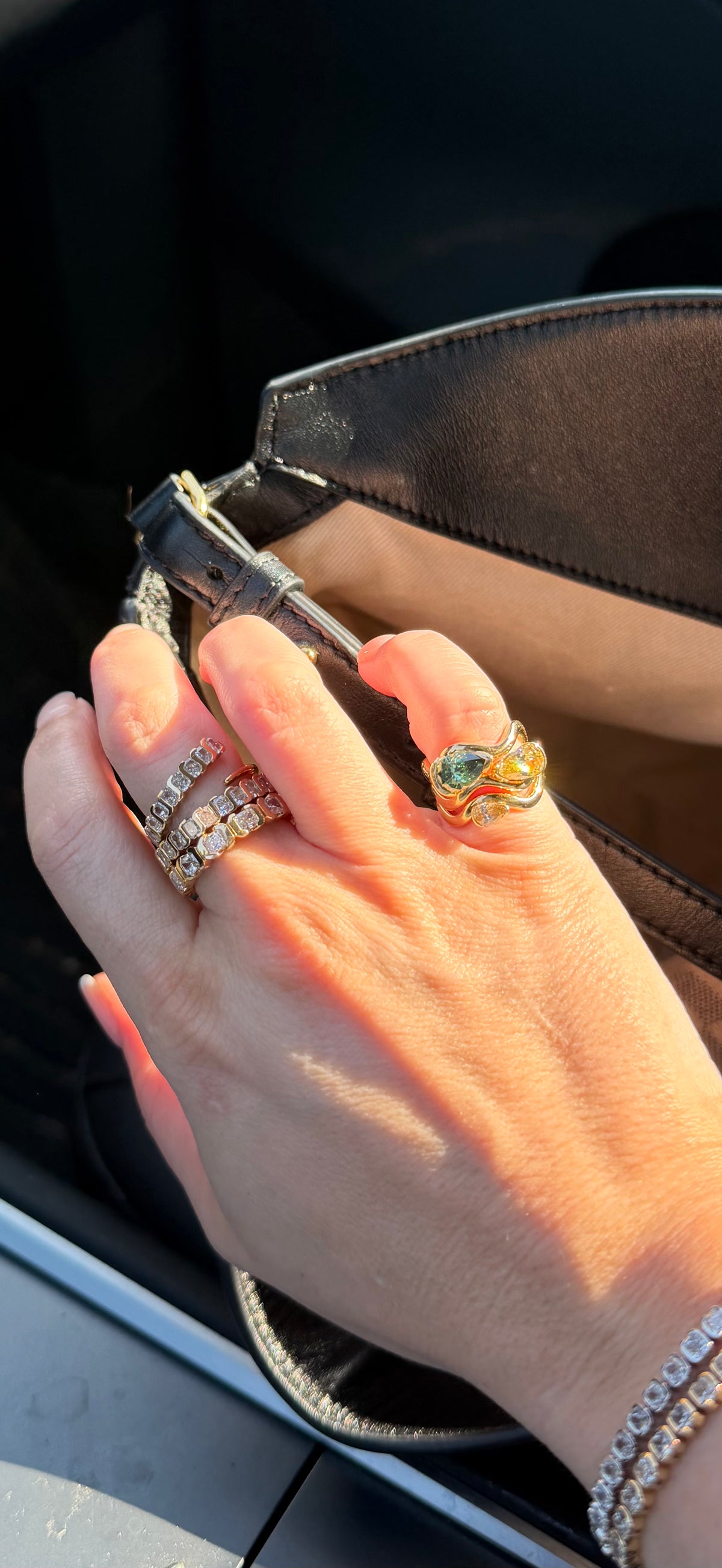 Hand with multiple rings holding a small black object, possibly a phone case, with a blurred background.