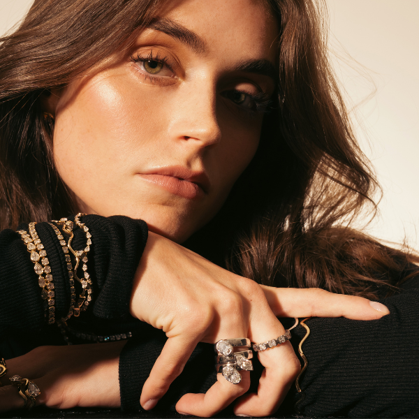 Woman wearing a black sweater with gold embellishments and multiple rings on her fingers.