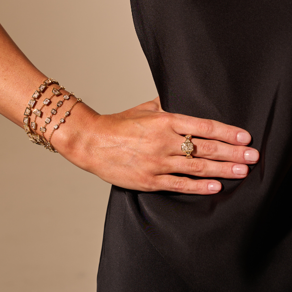 Hand wearing a gold ring and bracelet on a beige background