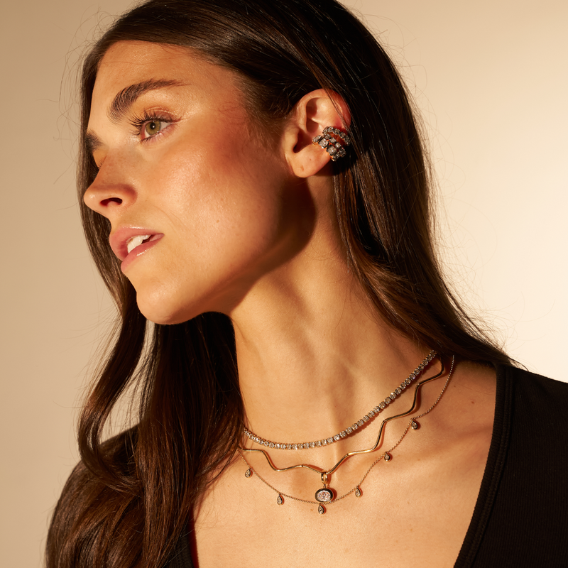 Woman wearing multiple necklaces and an earring against a neutral background