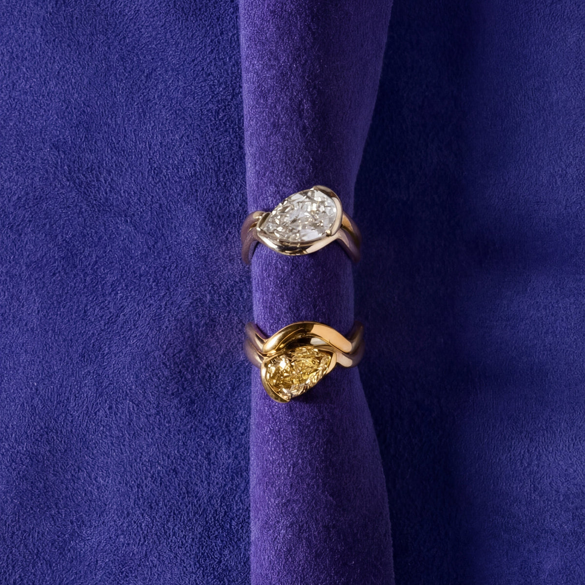 Pear-shaped diamond ring displayed upright in purple velvet fabric.