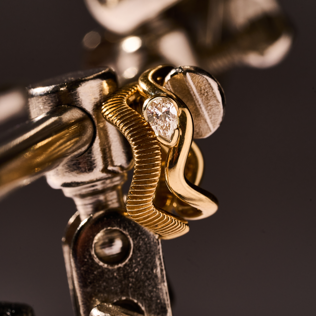 Close-up of a 0.2 CT pear-shaped lab diamond ring in an 18K yellow gold sculptural band on a jewelry tool.