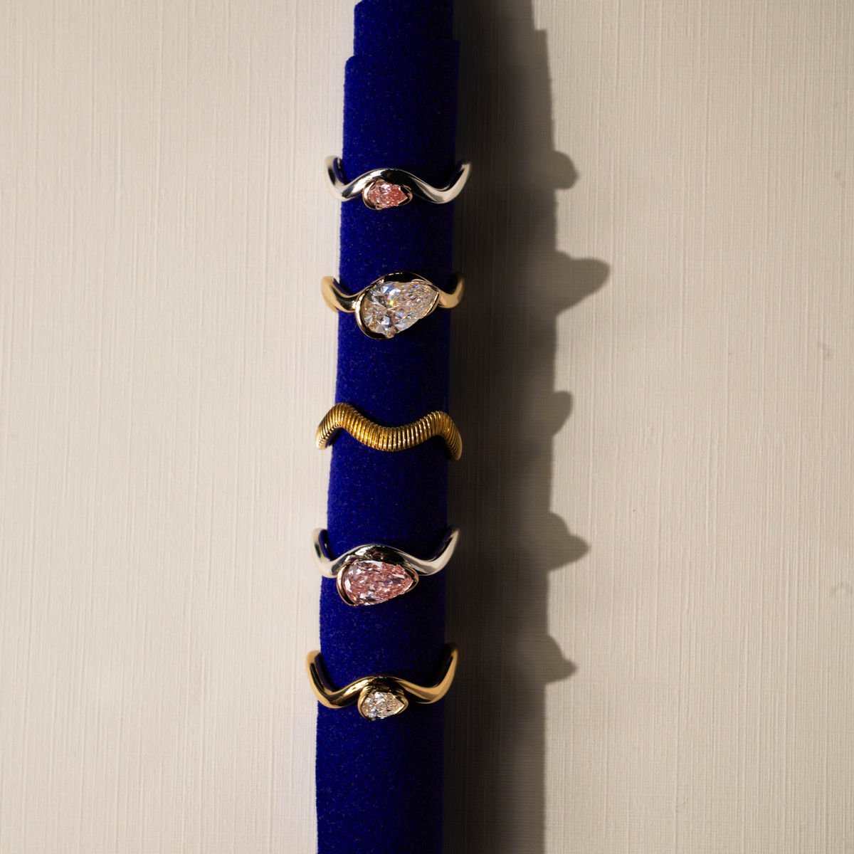 Set of gold rings with pink gemstones on a blue stand against a beige background