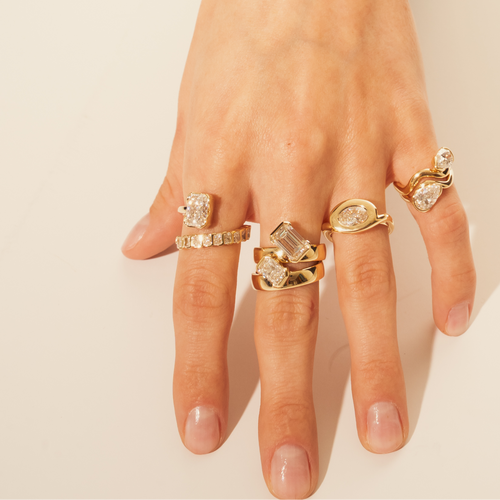 Hand wearing multiple gold rings with gemstones on a beige background