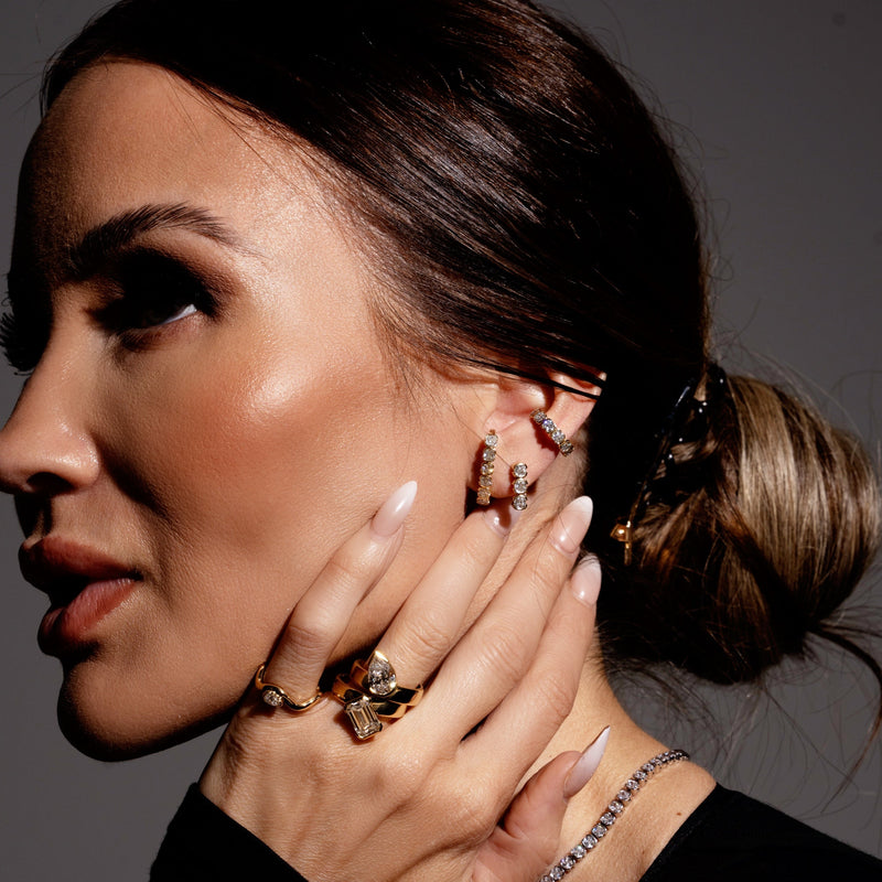Woman wearing diamond earrings and rings with a neutral background