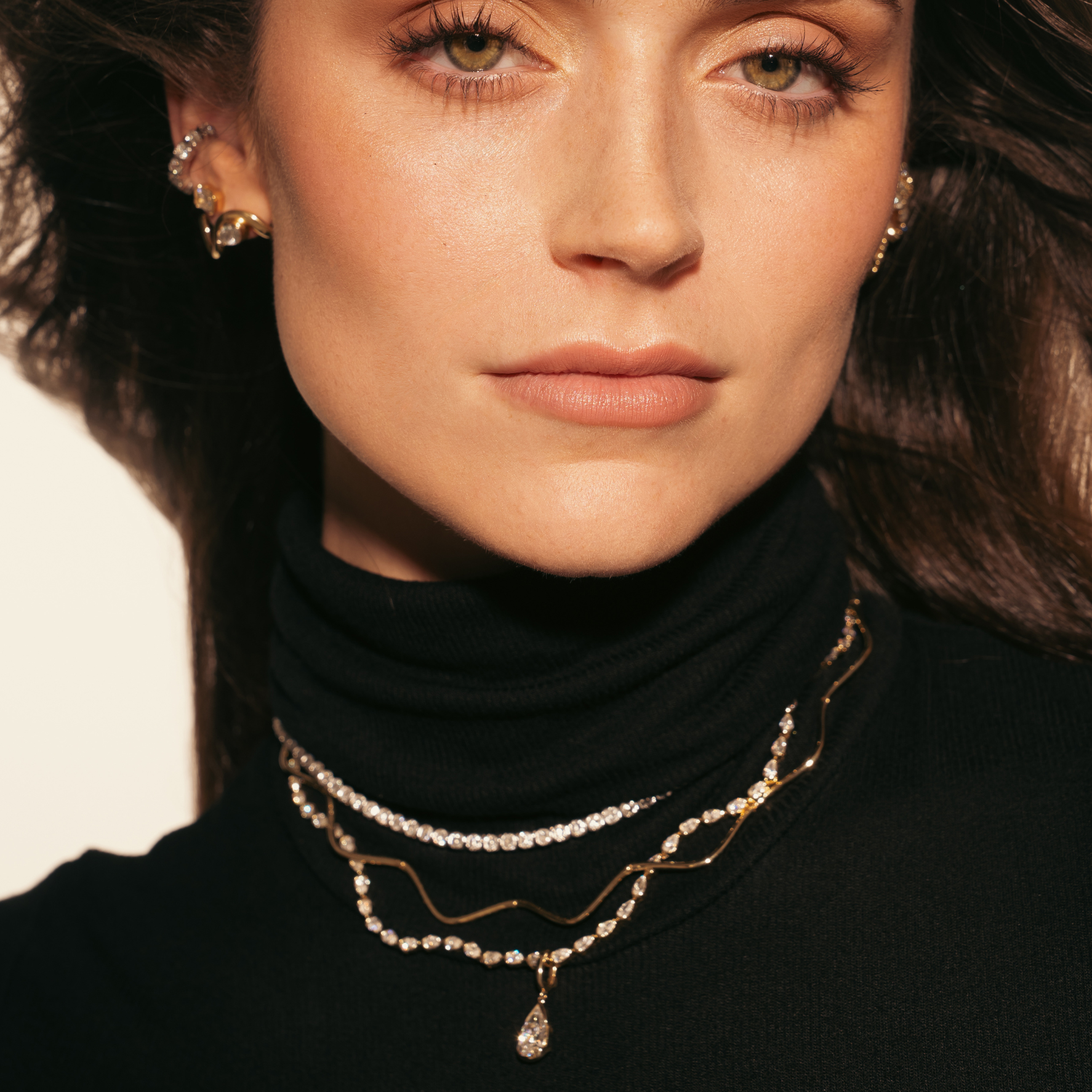 Close-up of a woman wearing multiple necklaces and earrings against a neutral background
