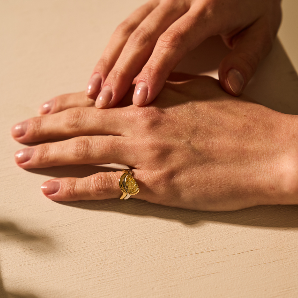 Close-up of hands wearing a yellow pear-shaped diamond ring in gold.